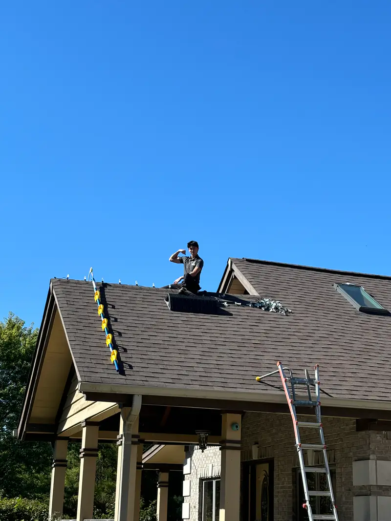 Installer on the roof above a front porch on a clear day, clips set along the gable edge